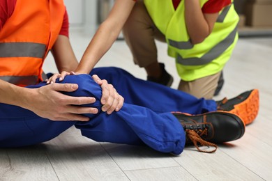 Photo of First aid. Man helping his injured colleague after work accident indoors, closeup