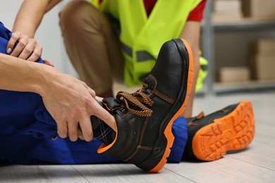 Photo of First aid. Man helping his injured colleague after work accident indoors, closeup