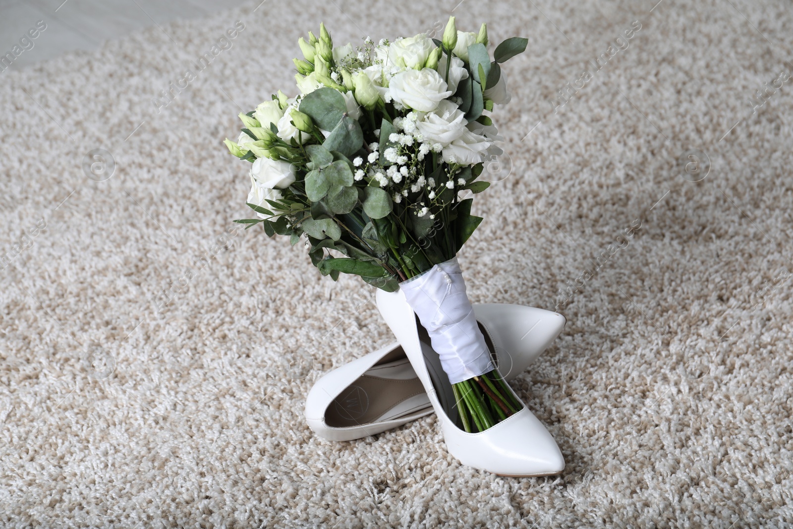 Photo of Wedding bouquet of beautiful flowers and bridal shoes on beige carpet, closeup