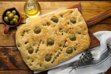 Photo of Delicious focaccia bread with olives, salt, thyme and oil on wooden table, flat lay