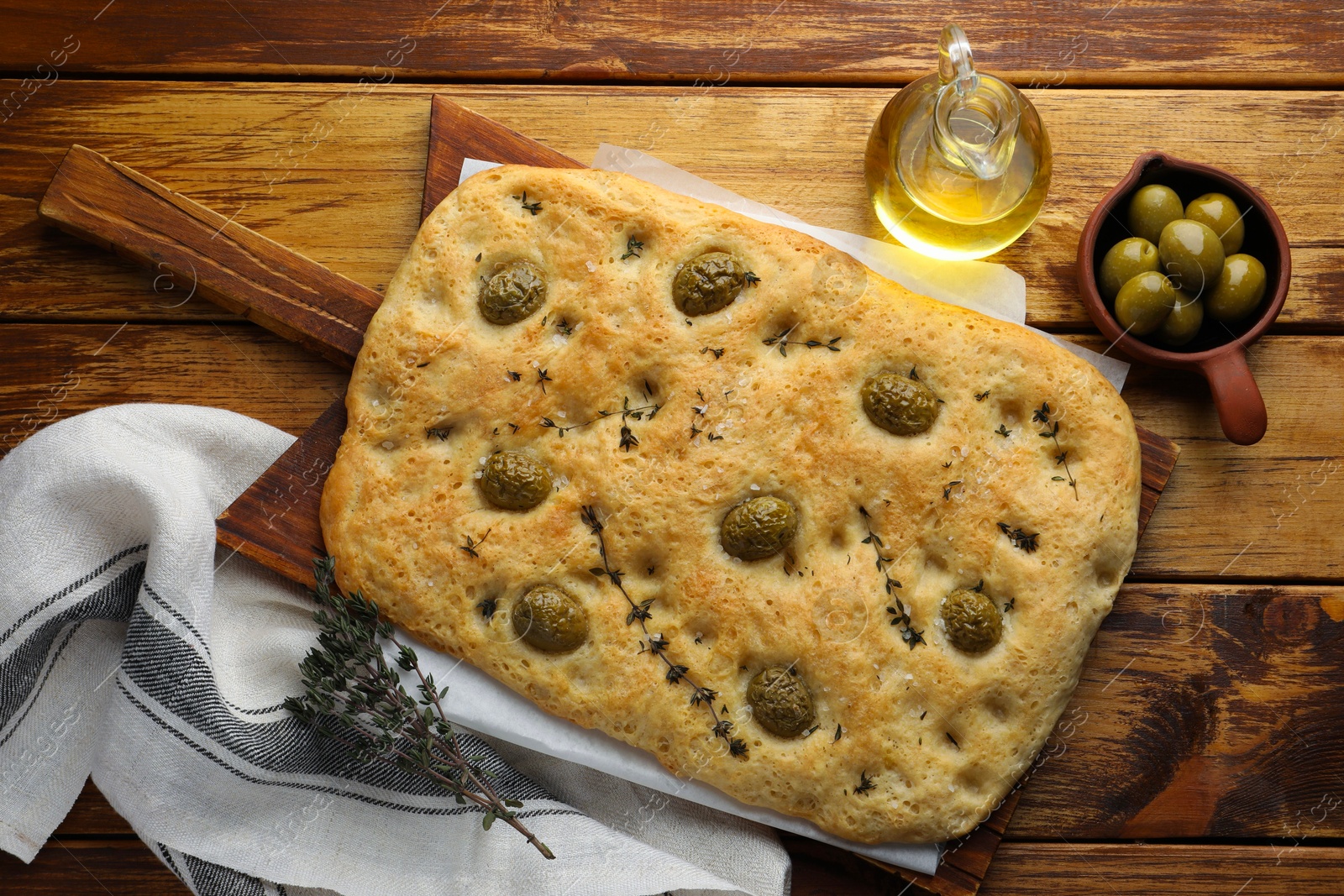 Photo of Delicious focaccia bread with olives, salt, thyme and oil on wooden table, flat lay