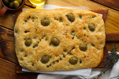 Photo of Delicious focaccia bread with olives, salt and thyme on wooden table, flat lay