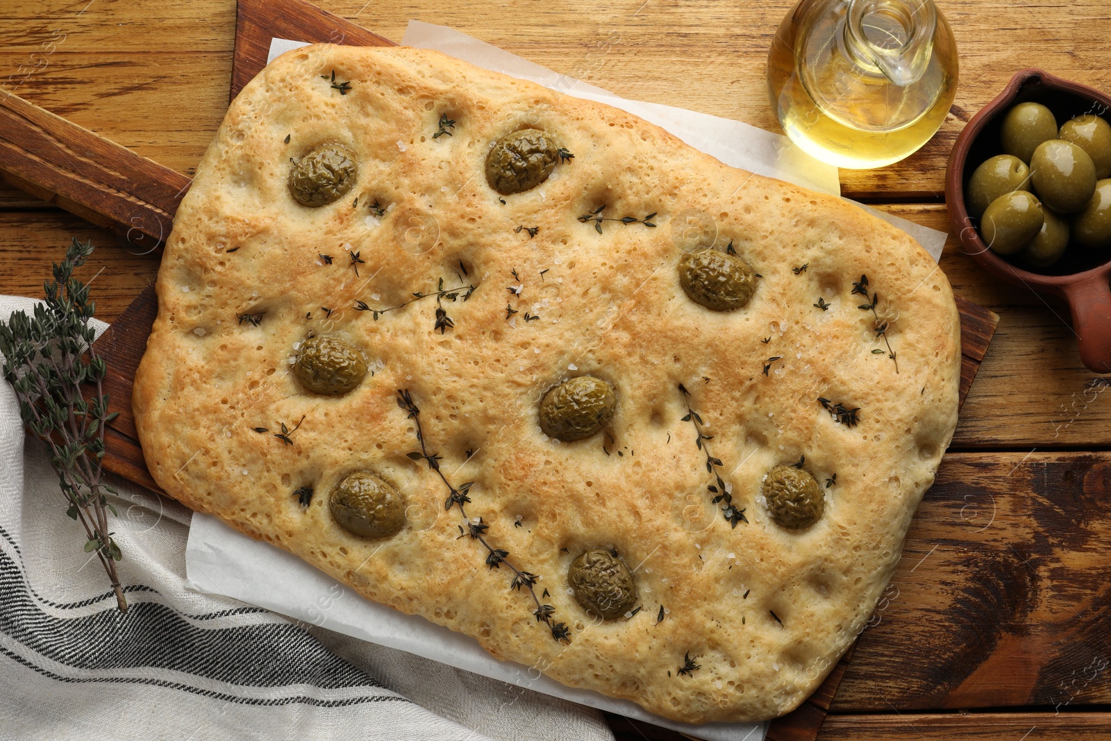 Photo of Delicious focaccia bread with olives, salt, thyme and oil on wooden table, flat lay