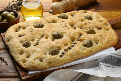 Photo of Delicious focaccia bread with olives, salt and thyme on wooden table, closeup