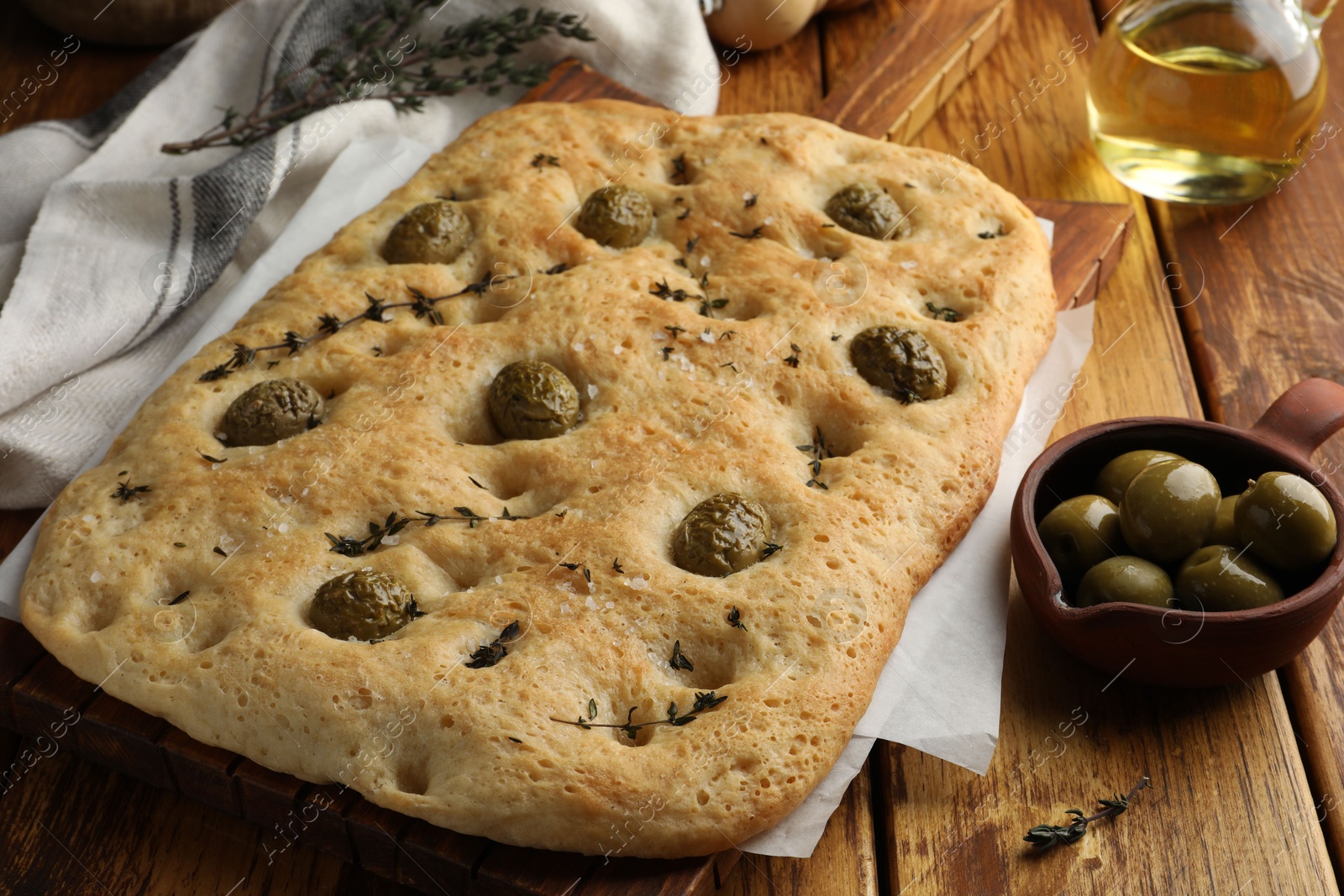 Photo of Delicious focaccia bread with olives, salt and thyme on wooden table, closeup