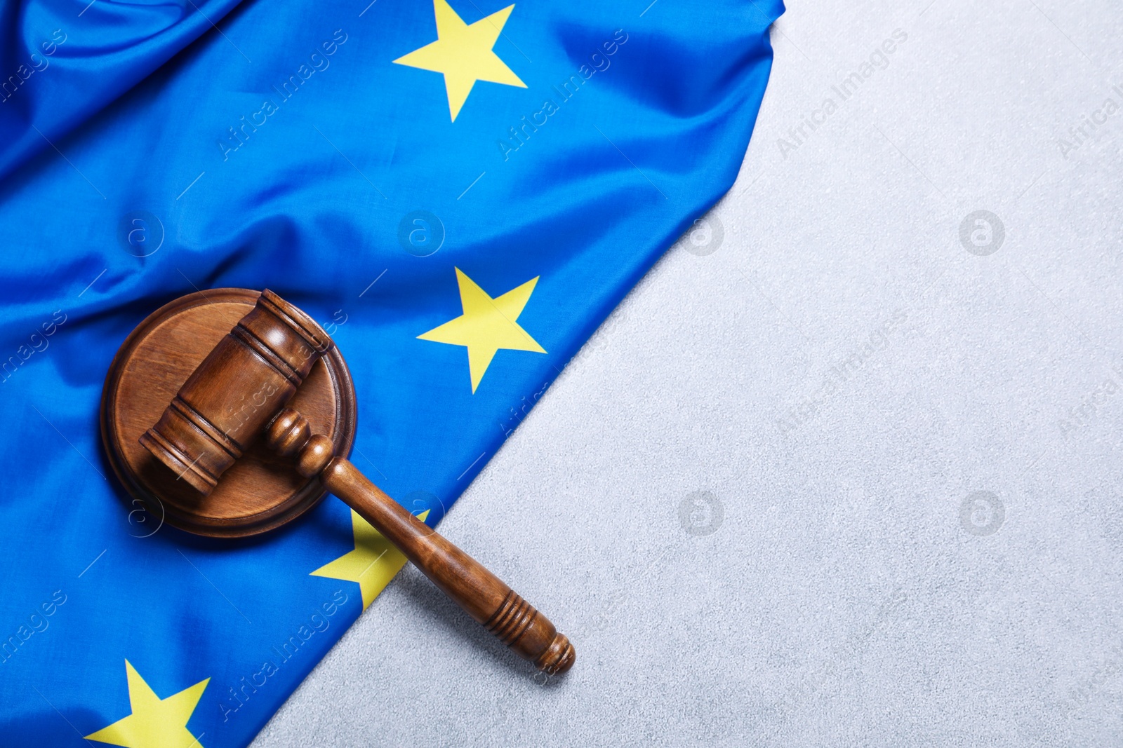 Photo of Judge's gavel and flag of European Union on light grey table, top view. Space for text