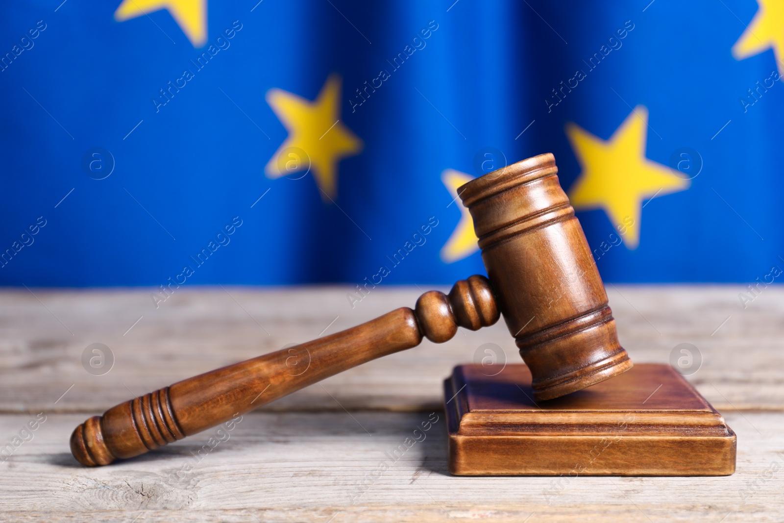 Photo of Judge's gavel on wooden table against European Union flag, closeup