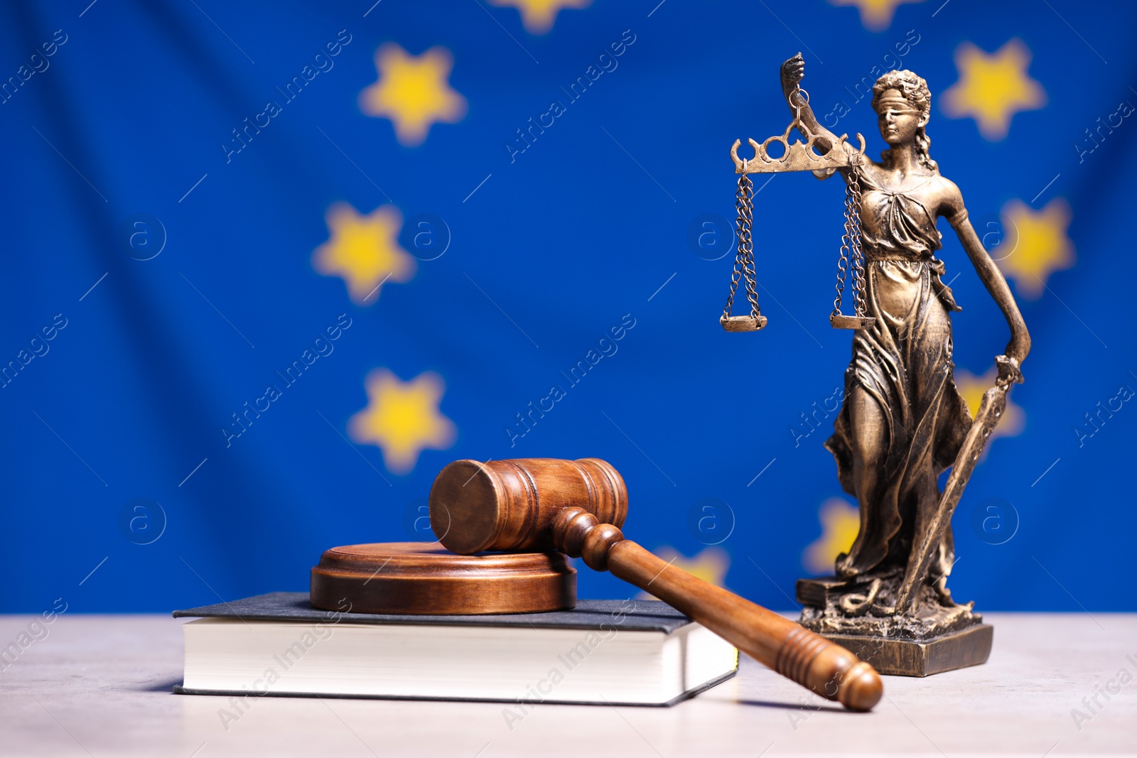 Photo of Figure of Lady Justice, judge's gavel and book on table against European Union flag