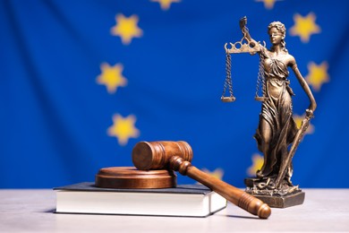 Photo of Figure of Lady Justice, judge's gavel and book on table against European Union flag