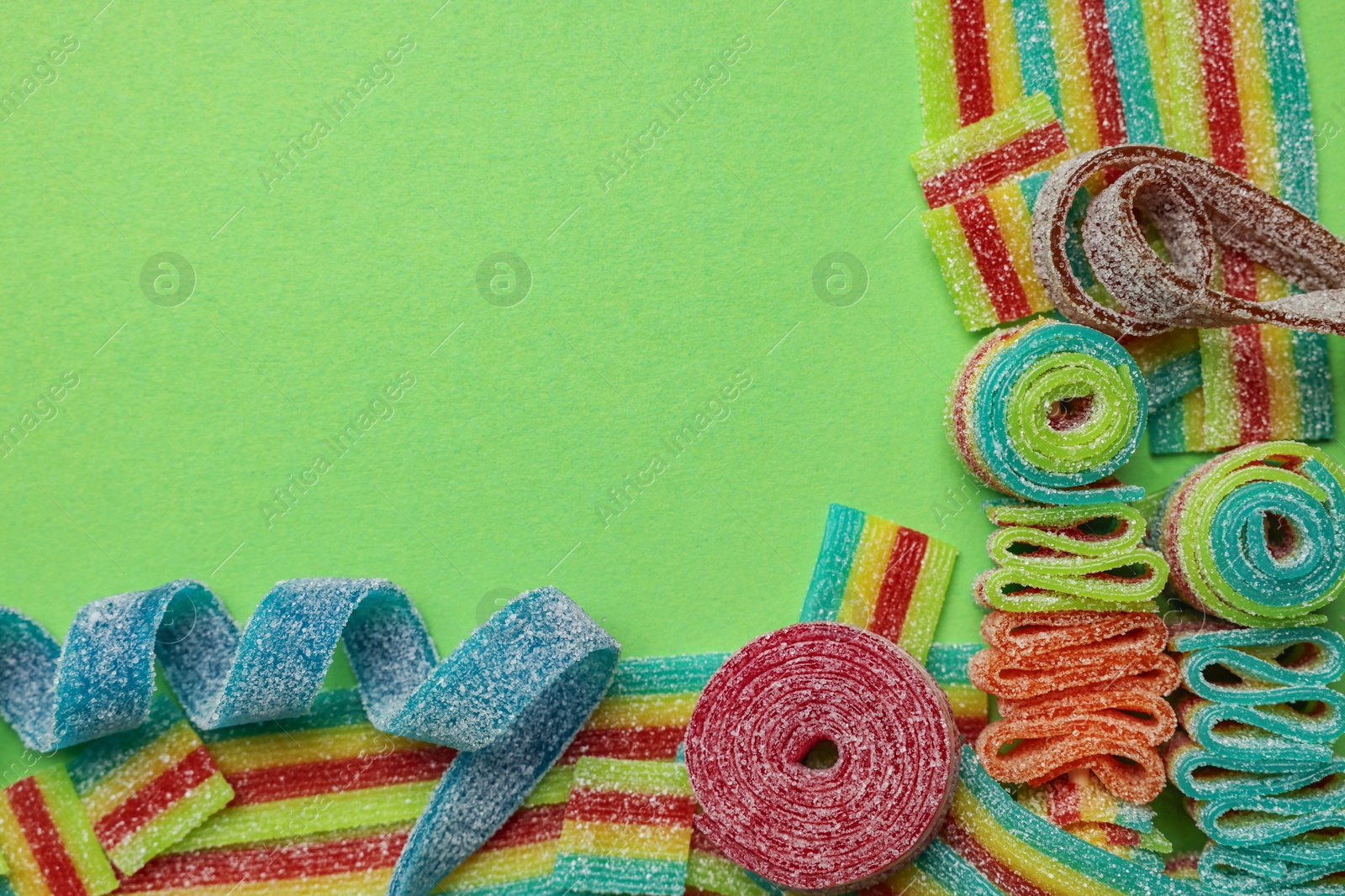 Photo of Different tasty sour belts on green background, flat lay. Space for text