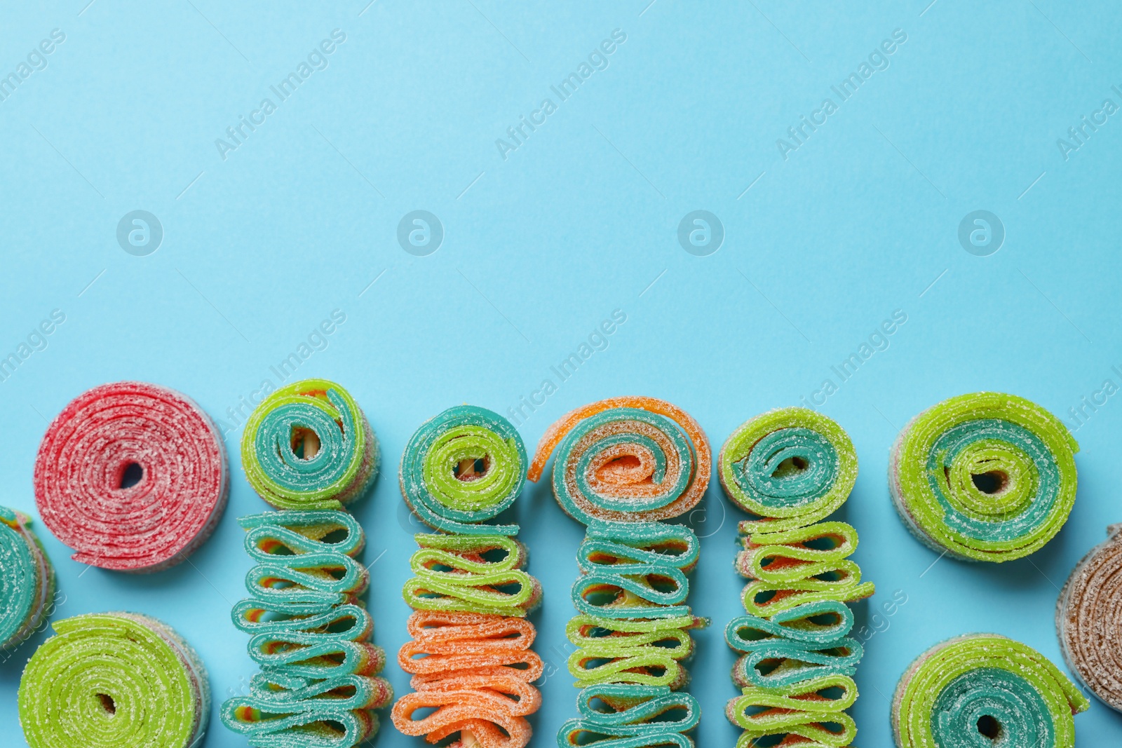 Photo of Different tasty sour belts on light blue background, flat lay. Space for text