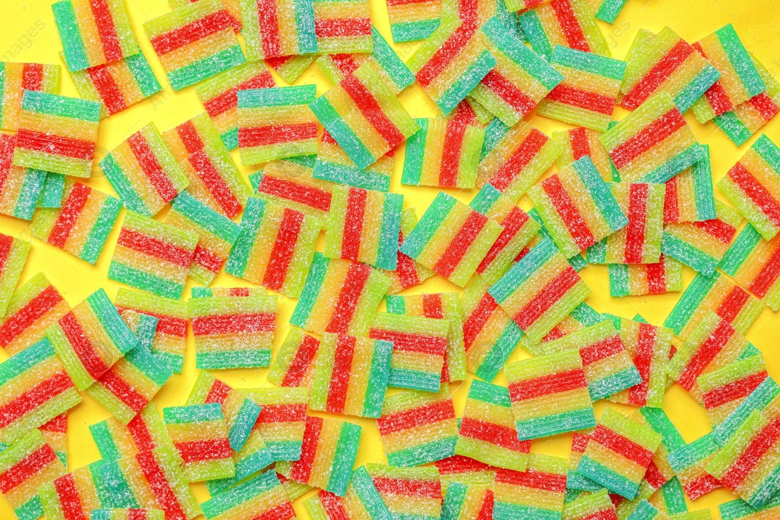 Photo of Tasty rainbow sour belts on yellow background, top view