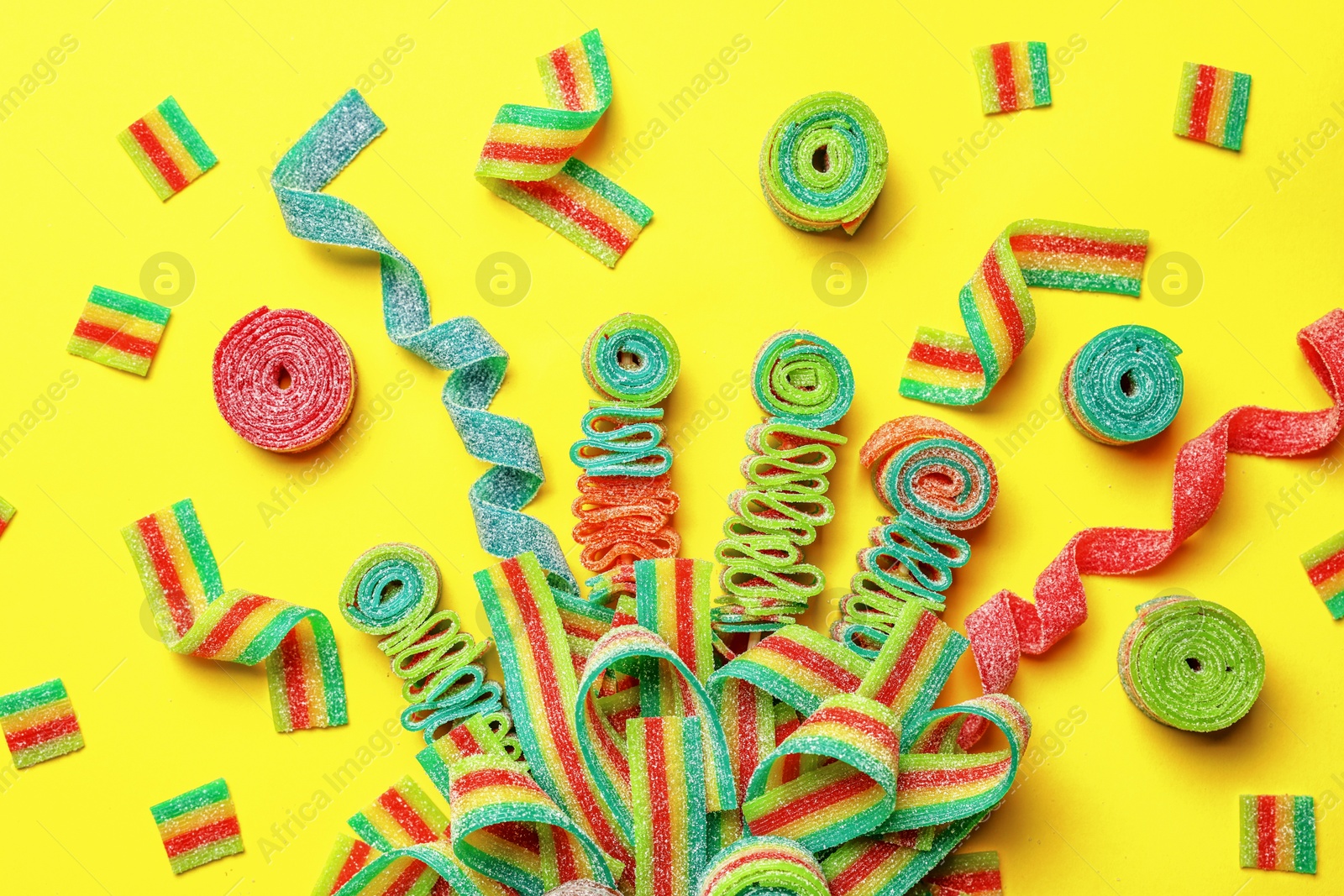 Photo of Different tasty sour belts on yellow background, flat lay