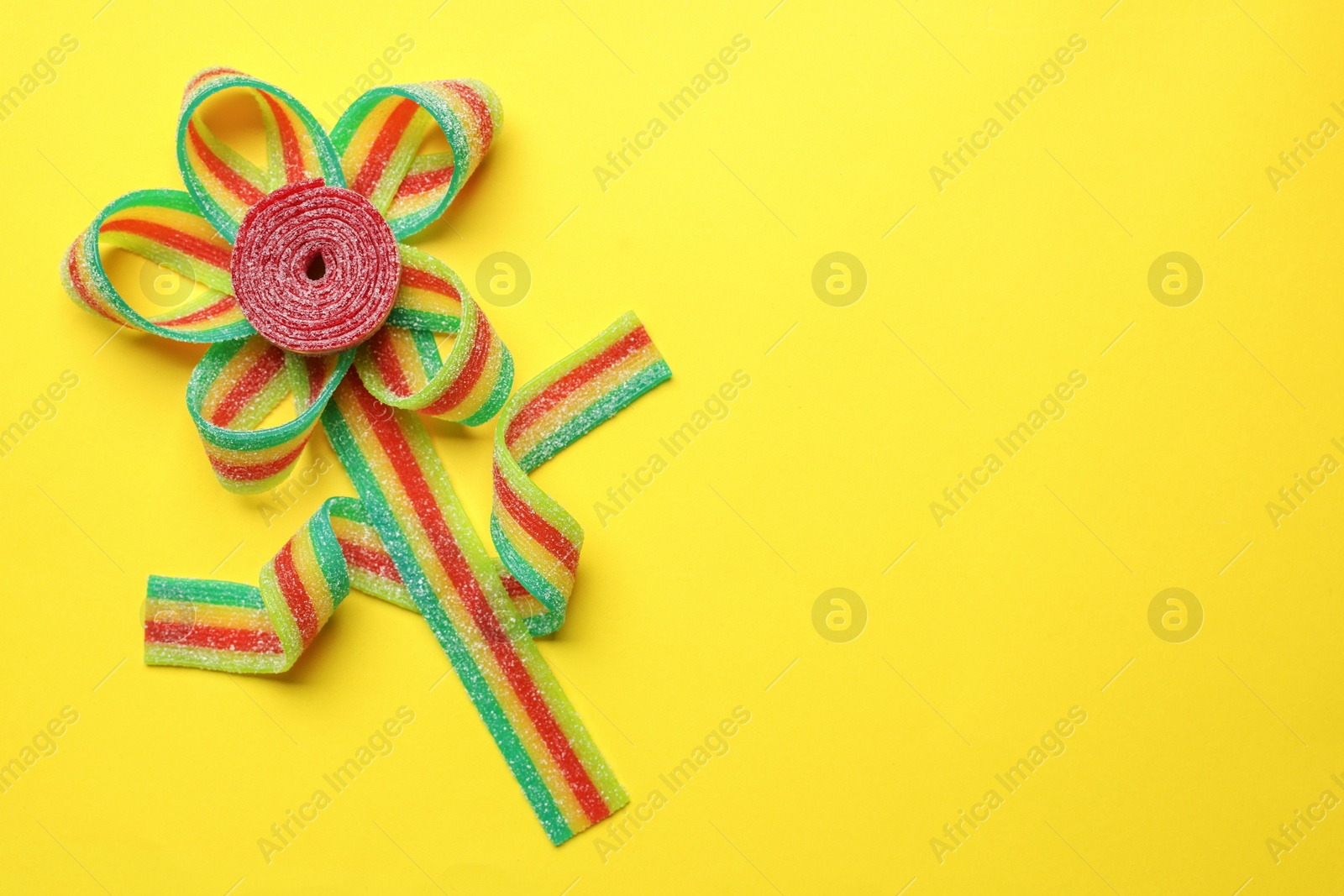 Photo of Flower made of tasty sour belts on yellow background, top view. Space for text