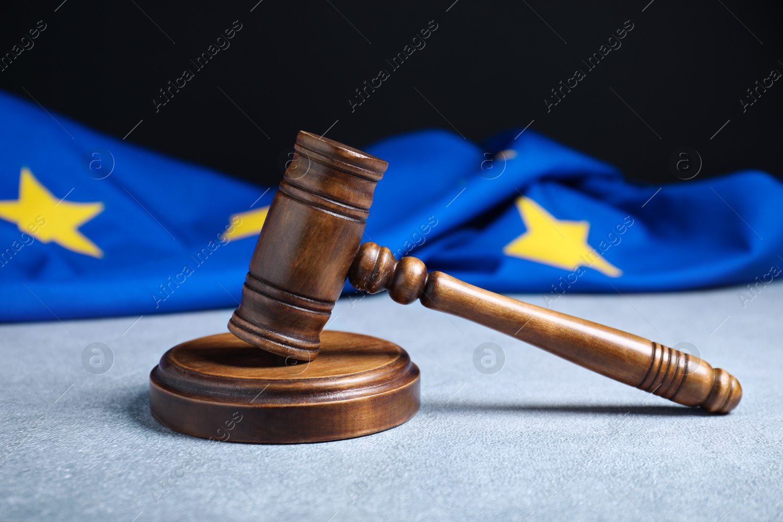 Photo of Judge's gavel and European Union flag on light textured table against black background, closeup