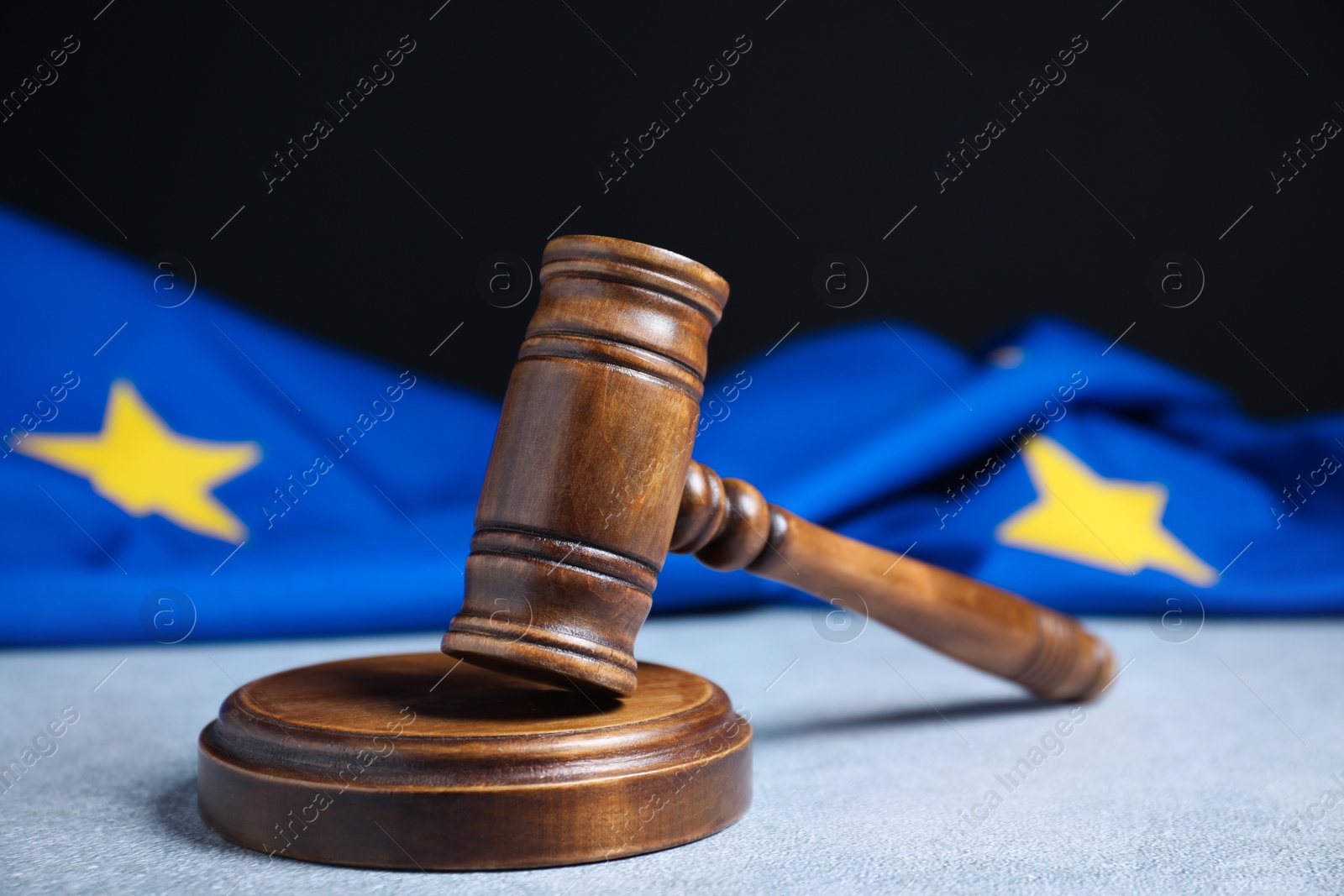 Photo of Judge's gavel and European Union flag on light textured table against black background, closeup