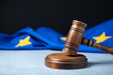 Photo of Judge's gavel and European Union flag on light textured table against black background, closeup. Space for text