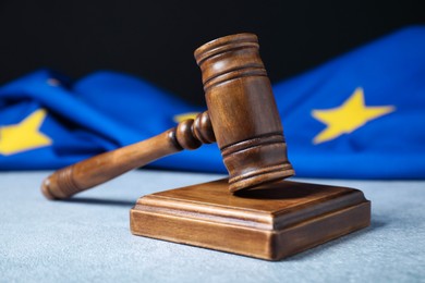 Photo of Judge's gavel and European Union flag on light textured table against black background, closeup