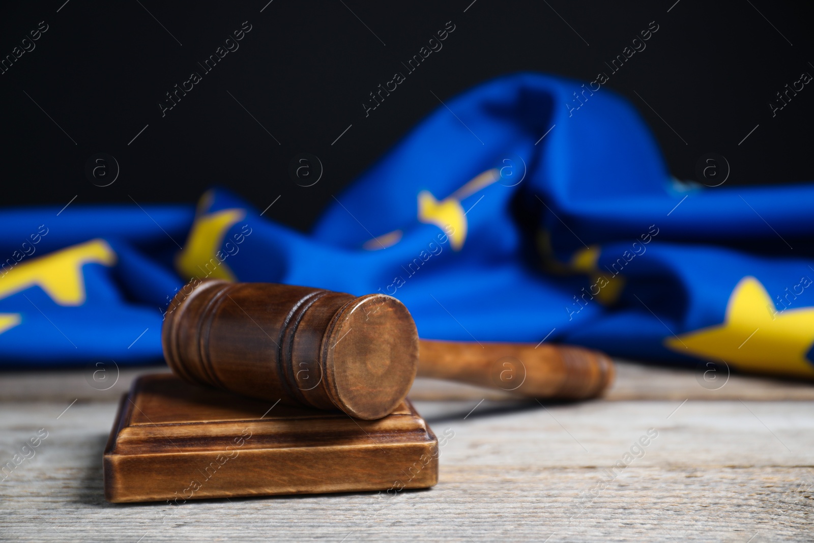 Photo of Judge's gavel and European Union flag on wooden table against black background, closeup