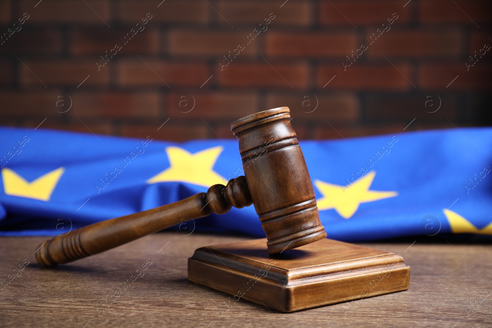 Photo of Judge's gavel and European Union flag on wooden table against brick wall, closeup