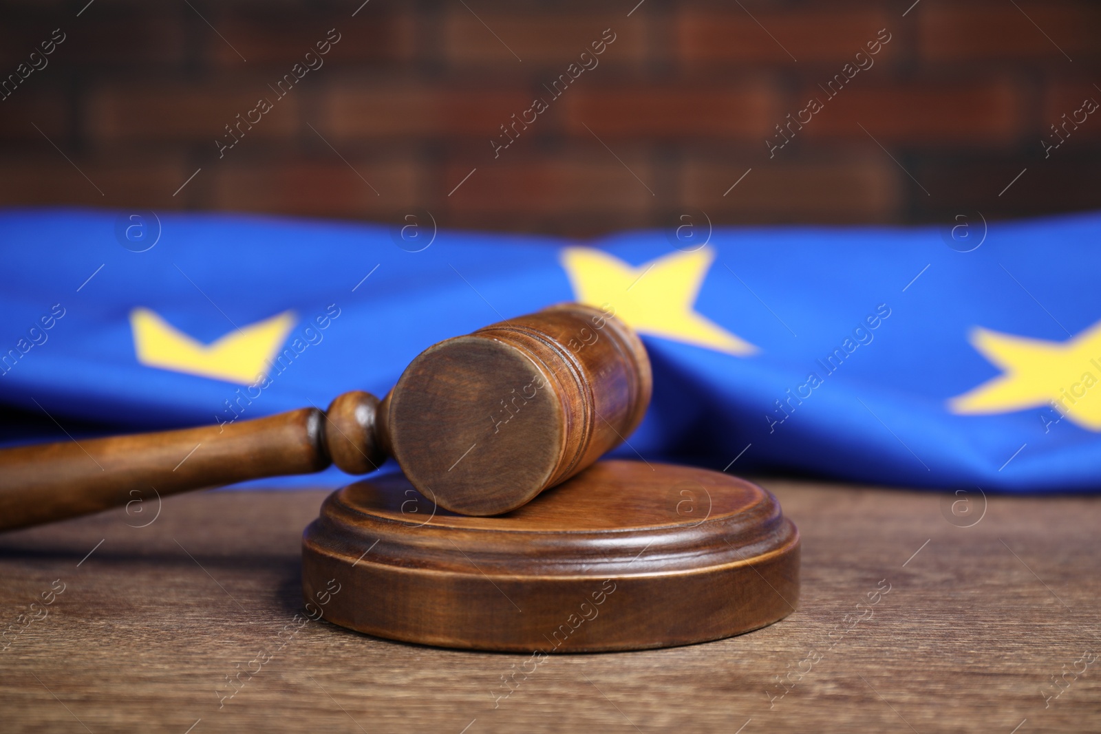 Photo of Judge's gavel and European Union flag on wooden table against brick wall, closeup