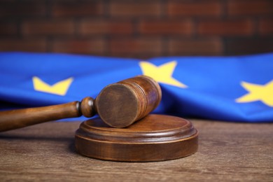 Photo of Judge's gavel and European Union flag on wooden table against brick wall, closeup