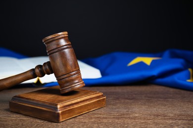 Photo of Judge's gavel and European Union flag on wooden table against black background, closeup. Space for text