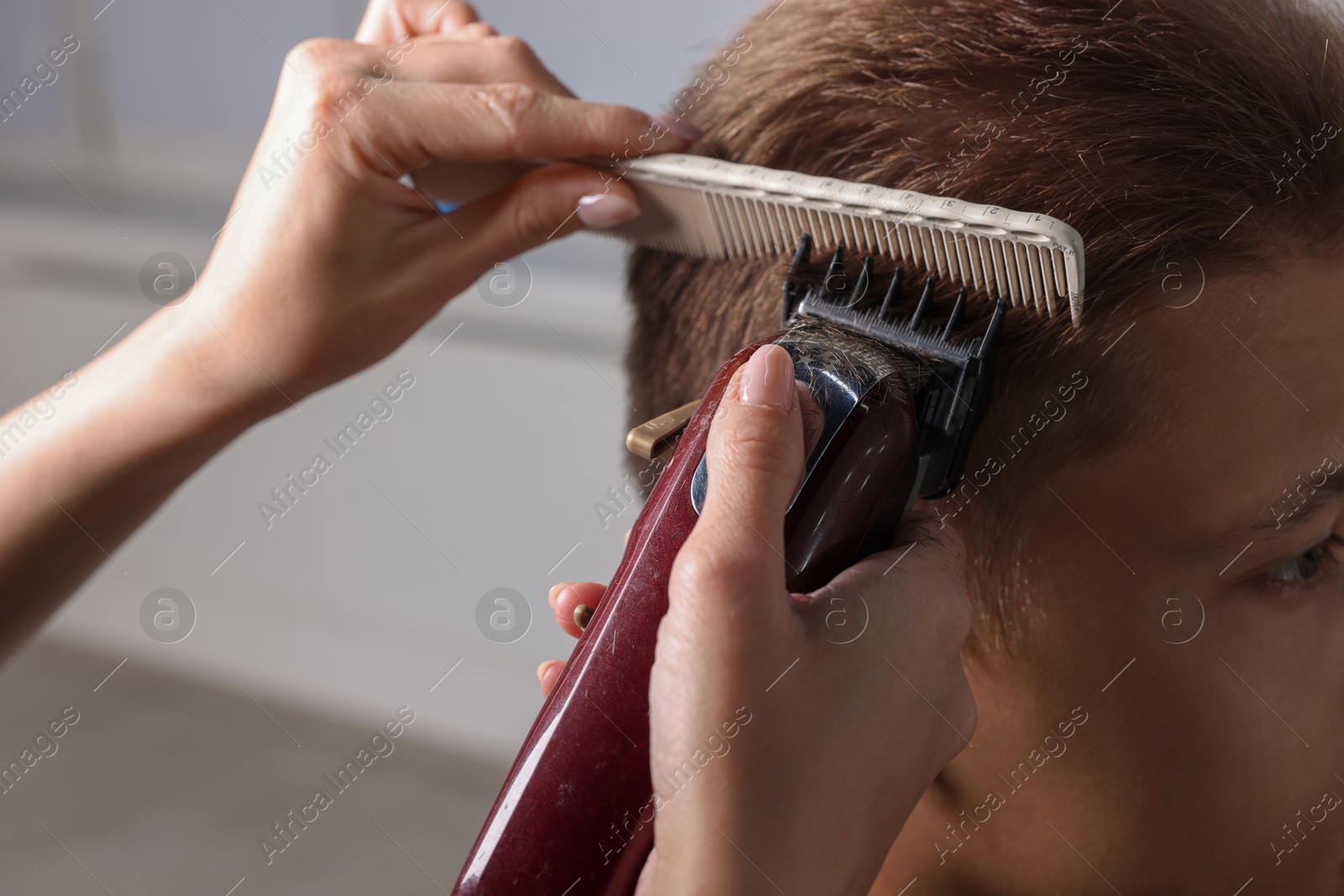 Photo of Professional barber making stylish haircut in salon, closeup