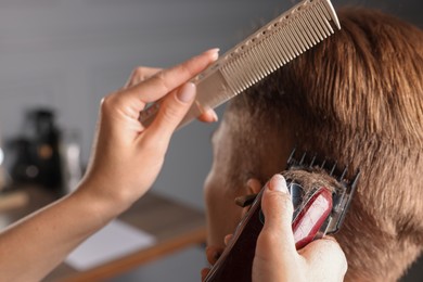 Photo of Professional barber making stylish haircut in salon, closeup