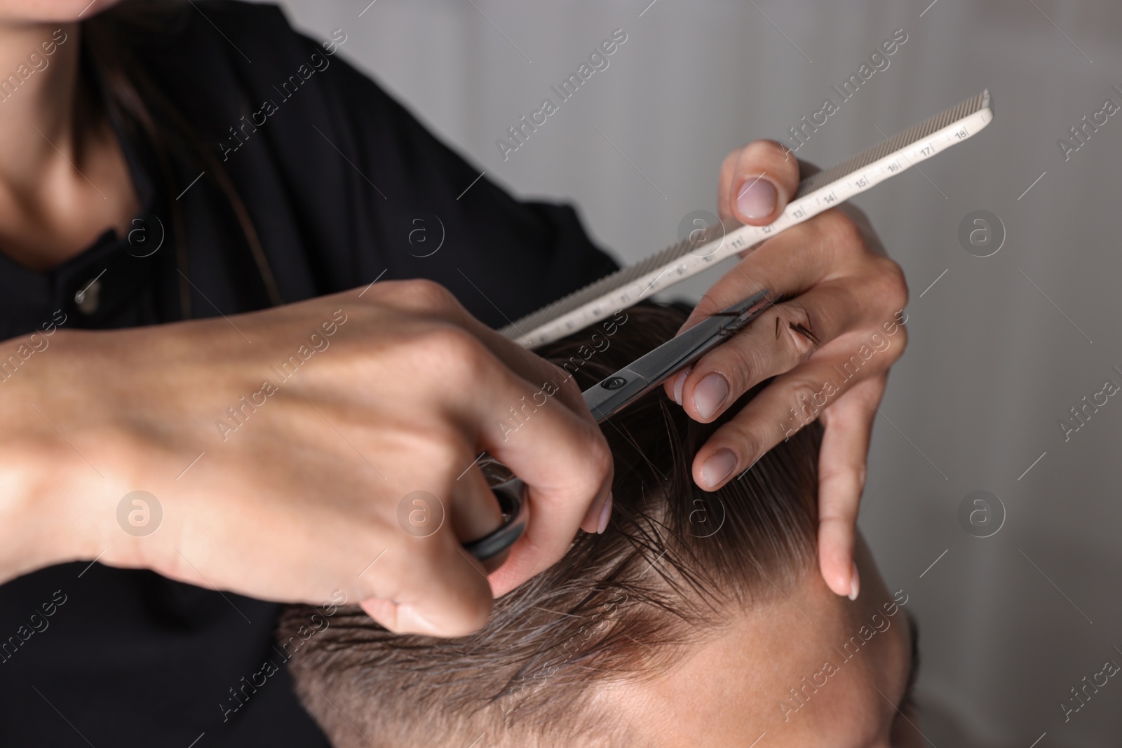 Photo of Professional hairdresser cutting client's hair with scissors in barbershop, closeup