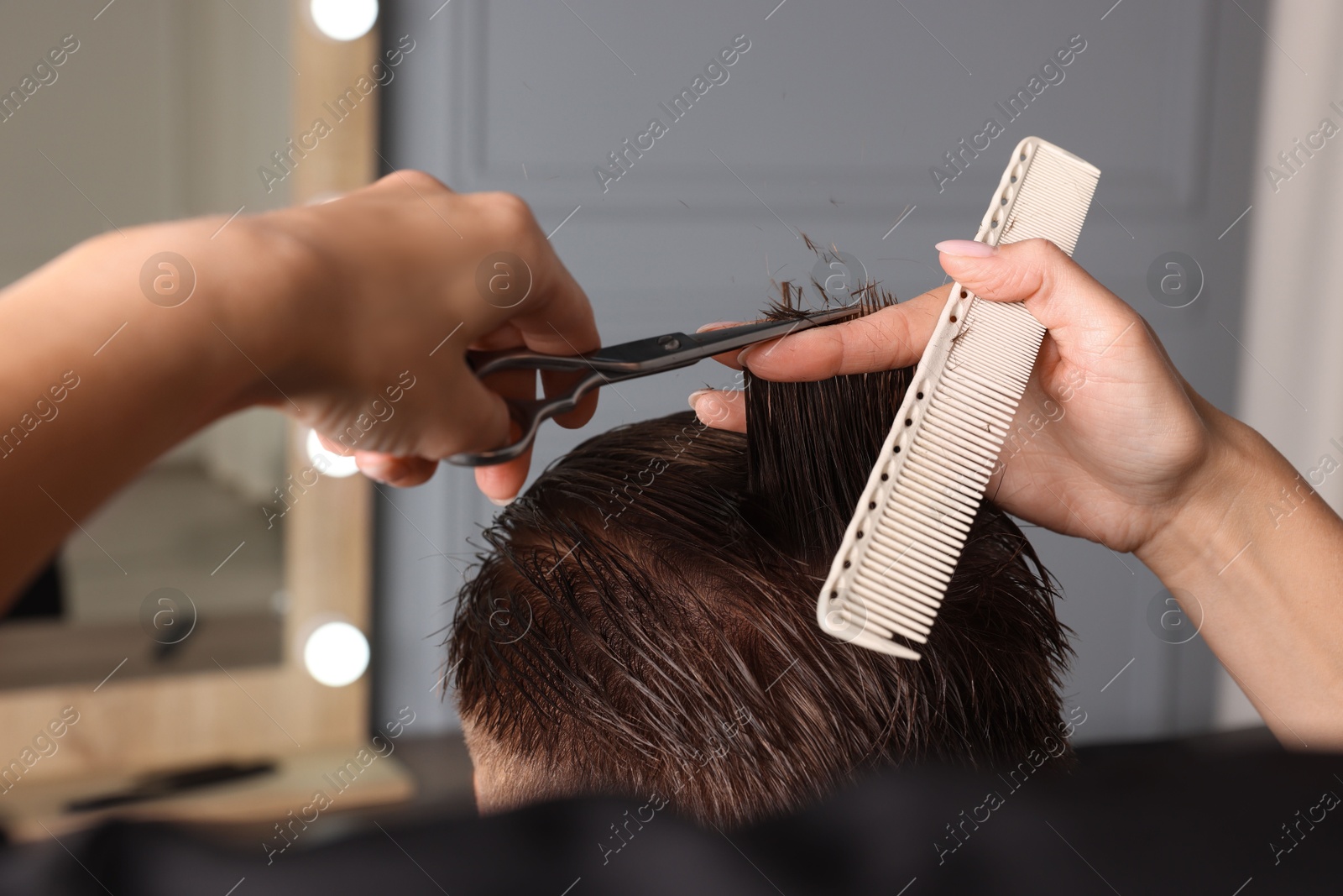 Photo of Professional hairdresser cutting client's hair with scissors in barbershop, closeup