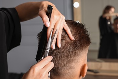 Photo of Professional hairdresser cutting client's hair with scissors in barbershop, closeup