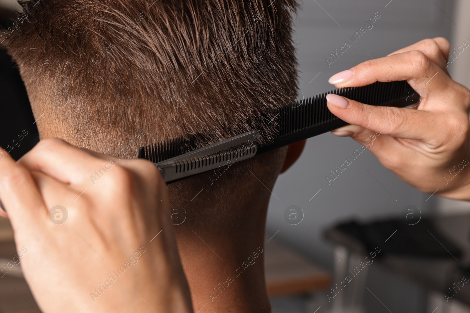 Photo of Professional hairdresser cutting client's hair with scissors in barbershop, closeup