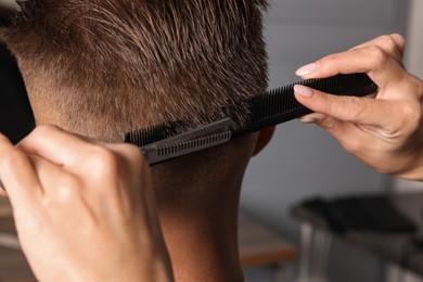 Photo of Professional hairdresser cutting client's hair with scissors in barbershop, closeup