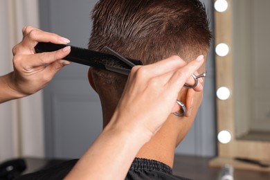 Photo of Professional hairdresser cutting client's hair with scissors in barbershop, closeup