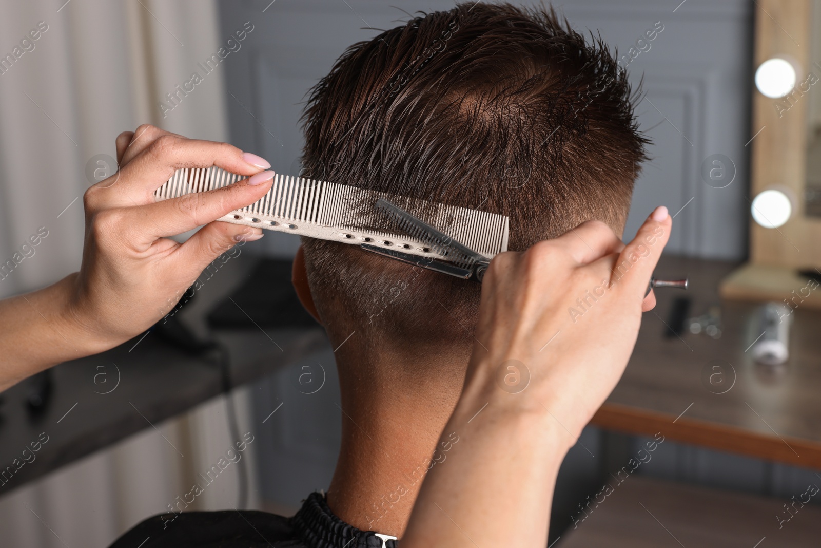 Photo of Professional hairdresser cutting client's hair with scissors in barbershop, closeup