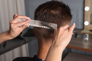 Photo of Professional hairdresser cutting client's hair with scissors in barbershop, closeup