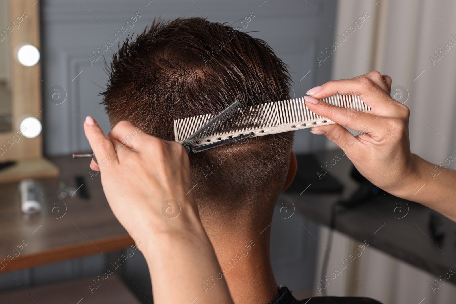 Photo of Professional hairdresser cutting client's hair with scissors in barbershop, closeup