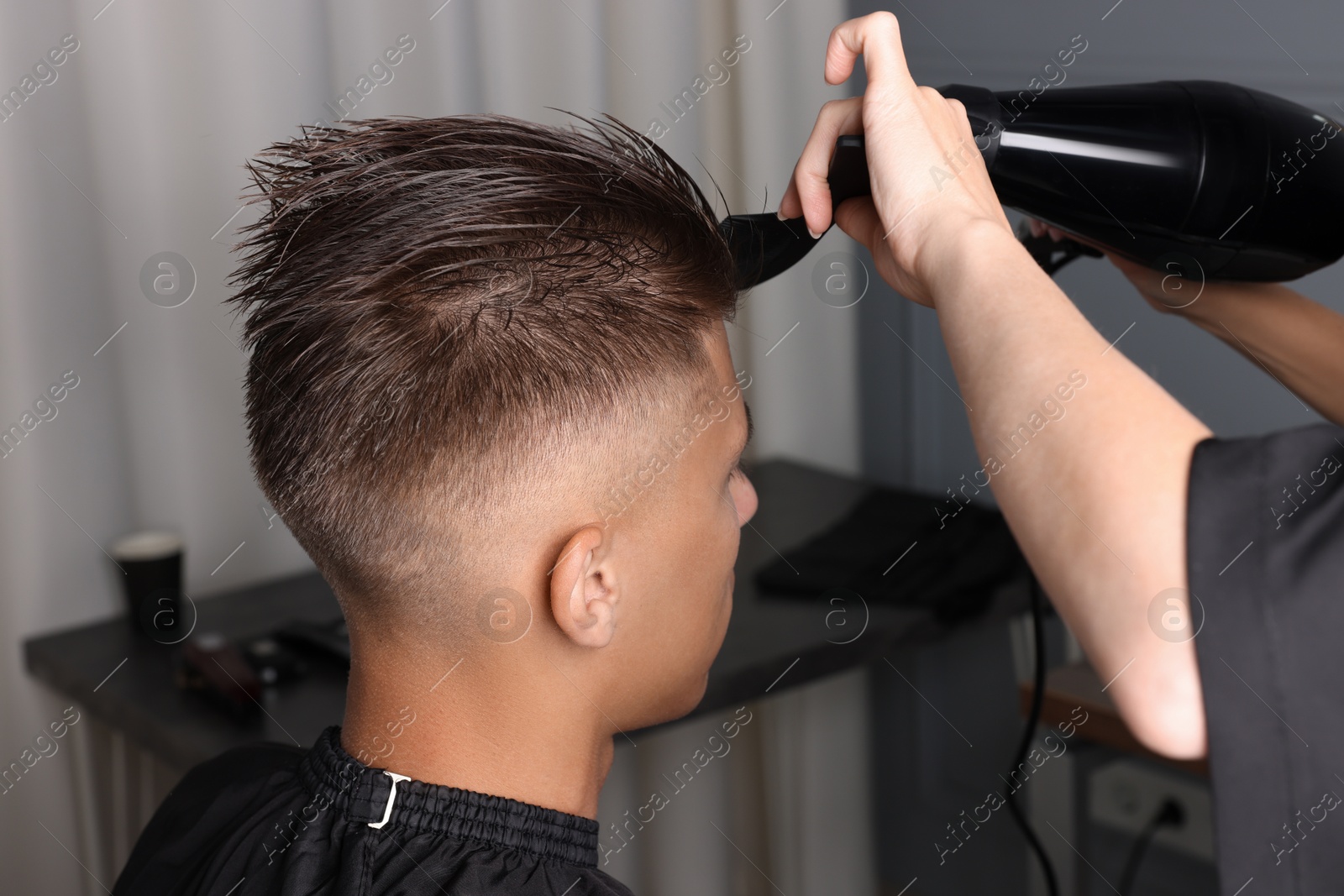 Photo of Hairdresser blow drying client's hair in barbershop, closeup