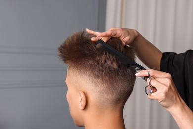 Photo of Professional barber making stylish haircut in salon, closeup