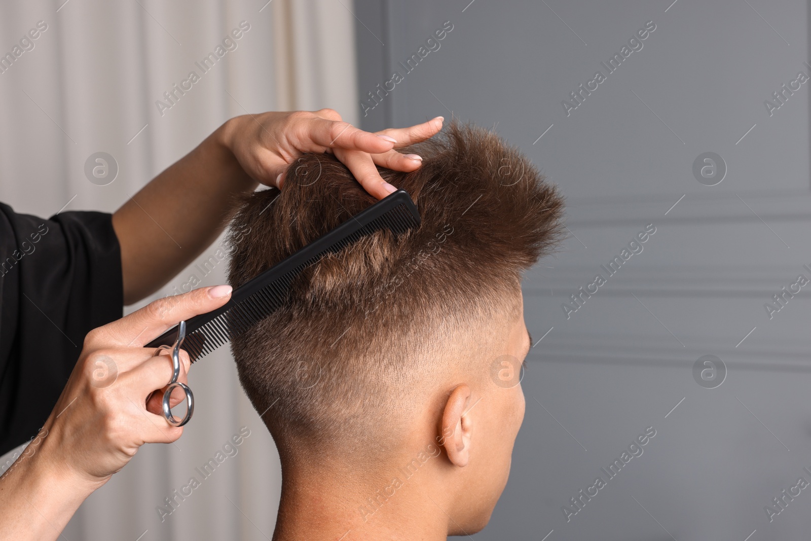 Photo of Professional barber making stylish haircut in salon, closeup