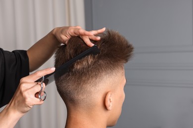 Photo of Professional barber making stylish haircut in salon, closeup