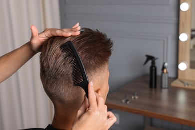 Photo of Hair cutting. Hairdresser combing man's hair in barbershop, closeup