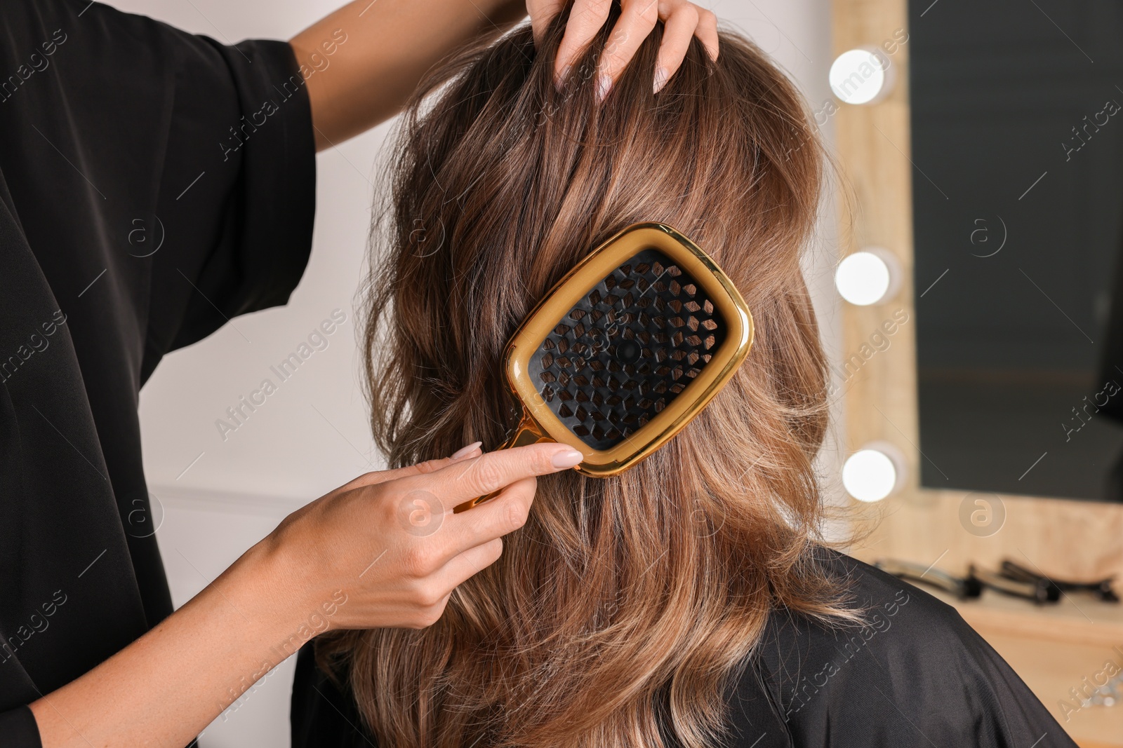 Photo of Hairdresser brushing client's hair in salon, closeup