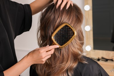 Photo of Hairdresser brushing client's hair in salon, closeup