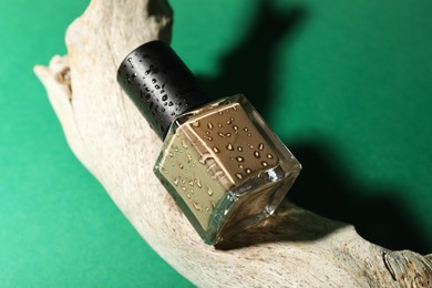 Photo of Nail polish in bottle and piece of decorative wood on green background, closeup