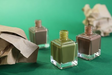 Nail polish in bottles and kraft paper on green background, closeup