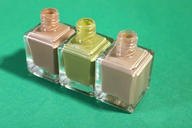 Photo of Nail polishes in bottles on green background, closeup