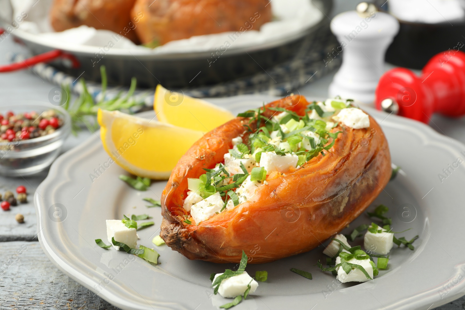 Photo of Tasty cooked sweet potato with feta cheese, lemon and green onion on table, closeup