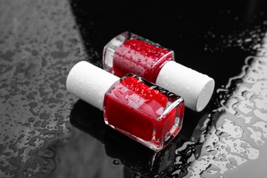 Nail polishes in bottles on wet dark surface, closeup